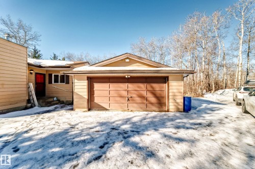 The property features a front door with a red frame, a window with dark shutters, and a garage with a brown door - 100 23016 Twp Rd 504, Rural Leduc County, AB - Outdoor