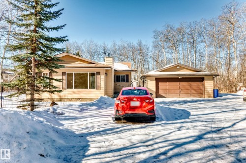 The property features a detached garage with a brown garage door, a light-colored exterior, and an expansive driveway - 100 23016 Twp Rd 504, Rural Leduc County, AB - Outdoor