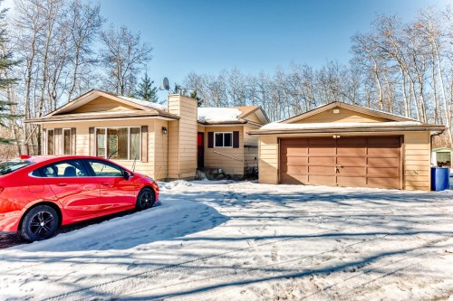 The property features a single-story residence with a light-colored exterior and a detached two-car garage with a brown door - 100 23016 Twp Rd 504, Rural Leduc County, AB - Outdoor