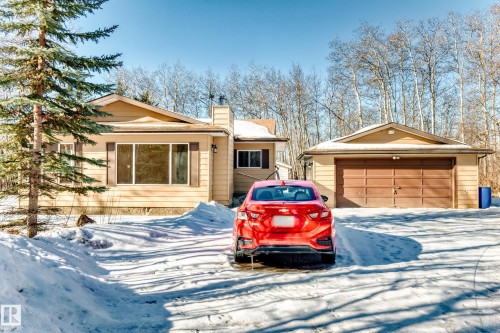 The property features a detached garage with a brown garage door, a light-colored exterior, and an expansive snow-covered driveway - 100 23016 Twp Rd 504, Rural Leduc County, AB - Outdoor