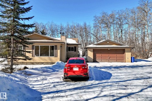The property features a detached garage with a brown double garage door, and a light-colored exterior with brown trim - 100 23016 Twp Rd 504, Rural Leduc County, AB - Outdoor