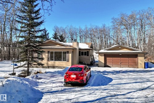 The property features a ranch-style home with a detached garage, set against a backdrop of bare trees - 100 23016 Twp Rd 504, Rural Leduc County, AB - Outdoor