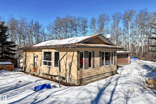 The property features a ranch-style exterior with wood siding, a brown shingle roof, and an attached garage with a wood-paneled door - 100 23016 Twp Rd 504, Rural Leduc County, AB - Outdoor