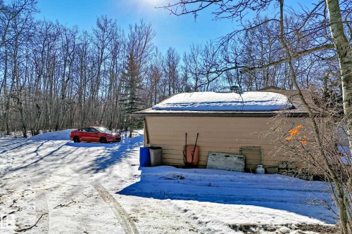 The property features an exterior with light-colored siding and a snow-covered roof, set against a backdrop of numerous bare trees - 100 23016 Twp Rd 504, Rural Leduc County, AB - Outdoor