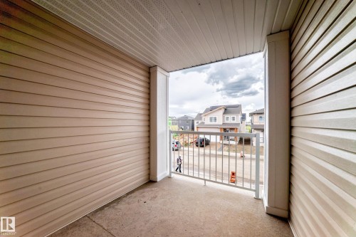 Covered concrete balcony featuring tan siding, white trim, and a white metal railing - 20415 16 Avenue, Edmonton, AB 