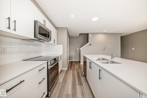 Modern kitchen featuring white cabinetry, light-toned countertops, stainless steel appliances, and a subway tile backsplash - 20415 16 Avenue, Edmonton, AB 