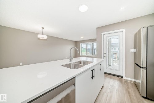 Kitchen island featuring a double basin stainless steel sink, a gooseneck faucet, and white countertops - 20415 16 Avenue, Edmonton, AB 