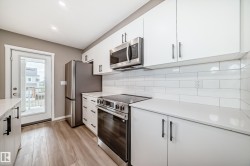 Modern kitchen featuring white cabinetry with black hardware, stainless steel appliances, light countertops, a white subway tile backsplash, and wood-finish flooring - 