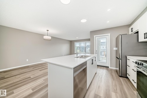 Open-concept kitchen featuring a large island with white countertops, stainless steel sink, and integrated dishwasher - 20415 16 Avenue, Edmonton, AB 