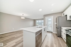 Open-concept kitchen featuring a large island with white countertops, stainless steel sink, and integrated dishwasher - 