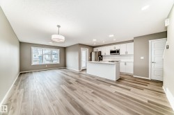 Open-concept living area featuring wood-finish flooring, a white kitchen island, stainless steel appliances, white cabinetry, and recessed lighting - 