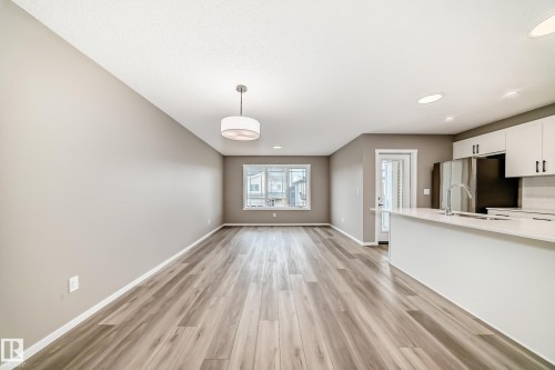 Open-concept living area featuring wood-finish flooring, a modern chandelier, and a kitchen island with an undermount sink - 20415 16 Avenue, Edmonton, AB 