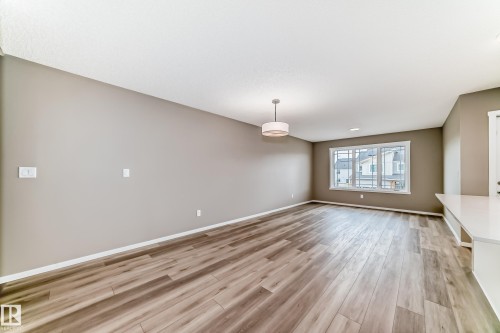 Open living space featuring wood-finish flooring, neutral-toned walls, and a contemporary ceiling light fixture - 20415 16 Avenue, Edmonton, AB 