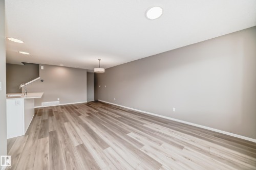 Spacious room featuring wood-finish flooring, recessed lighting, and a contemporary pendant light fixture - 20415 16 Avenue, Edmonton, AB 