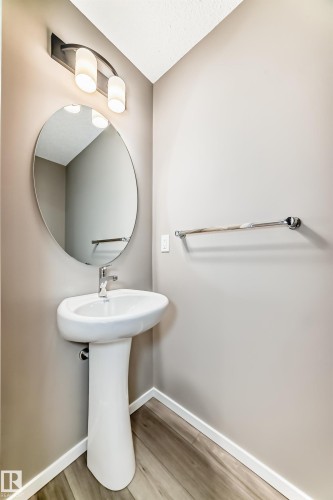 Pedestal sink with chrome faucet, oval wall mirror, and modern vanity lighting - 20415 16 Avenue, Edmonton, AB 