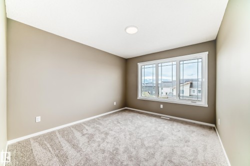 Neutral-toned room featuring a large triple window with white trim, recessed ceiling lighting, and a textured gray carpet - 20415 16 Avenue, Edmonton, AB 