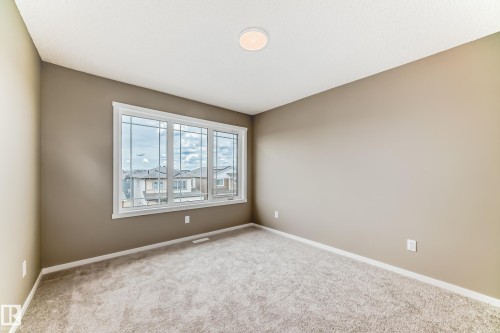 Spacious room featuring a large triple-pane window with white trim, neutral-toned carpeting, and light brown wall paint - 20415 16 Avenue, Edmonton, AB 
