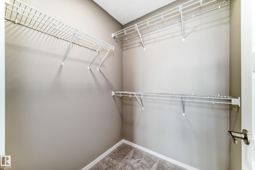 Walk-in closet featuring neutral-toned walls, white wire shelving, white trim, and textured carpet flooring - 20415 16 Avenue, Edmonton, AB 