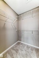 Walk-in closet featuring wire shelving, wall-mounted hanging rods, light gray wall paint, white baseboards, and gray carpet flooring - 