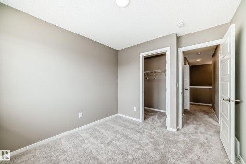 Neutral-toned bedroom featuring plush gray carpeting, a built-in closet with wire shelving, and crisp white trim - 20415 16 Avenue, Edmonton, AB 