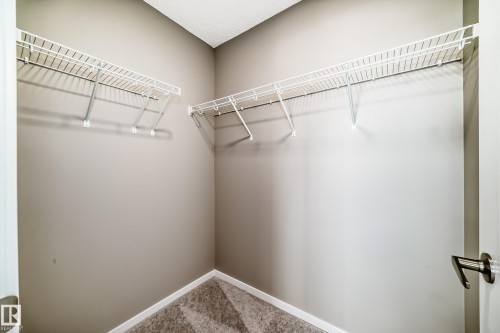 Walk-in closet featuring neutral-toned walls, white wire shelving, white baseboards, and patterned carpet - 20415 16 Avenue, Edmonton, AB 