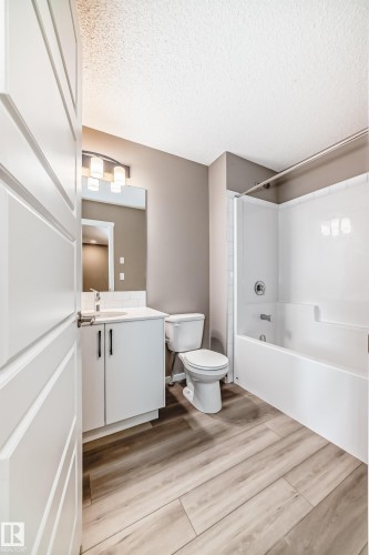 Full bathroom with wood-finish flooring, white vanity with integrated sink, modern wall-mounted light fixture, and a white tub/shower combination - 20415 16 Avenue, Edmonton, AB 