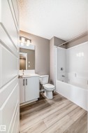 Full bathroom with wood-finish flooring, white vanity with integrated sink, modern wall-mounted light fixture, and a white tub/shower combination - 