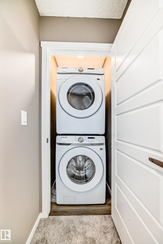 Stackable laundry units within a dedicated closet space, featuring wood-finish flooring and integrated overhead lighting - 20415 16 Avenue, Edmonton, AB 