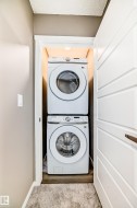 Stackable laundry units within a dedicated closet space, featuring wood-finish flooring and integrated overhead lighting - 