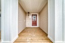 Covered front porch featuring wood-finish flooring, white architectural columns, beige vinyl siding, and a red entry door with decorative glass - 20415 16 Avenue, Edmonton, AB 