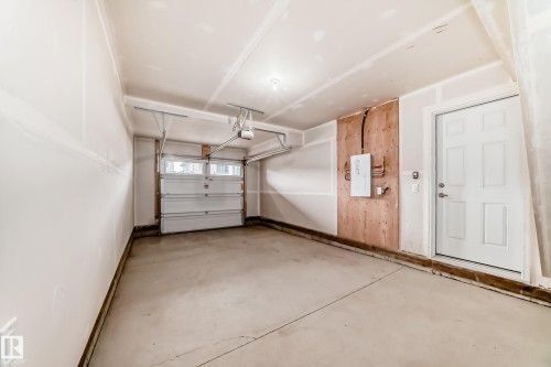 Spacious garage featuring a concrete floor, an overhead garage door with upper window panels, and a ceiling-mounted garage door opener - 20415 16 Avenue, Edmonton, AB 