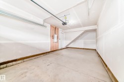 Spacious garage featuring a concrete floor, white drywall walls, ceiling-mounted garage door opener, and a utility panel on a wood-paneled section - 