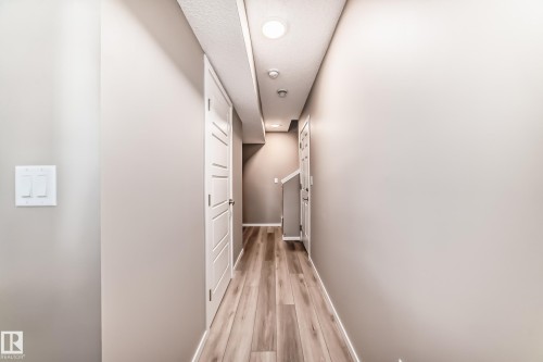 Hallway featuring wood-finish flooring, light neutral wall paint, and white trim - 20415 16 Avenue, Edmonton, AB 