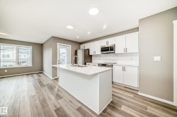 Modern kitchen featuring a central island with a sink, stainless steel appliances, white cabinetry, a subway tile backsplash, and wood-finish flooring - 