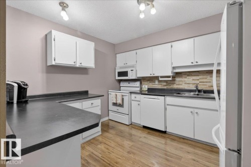 The property features a kitchen with white cabinetry, dark countertops, and a tiled backsplash - 3240 130A Avenue, Edmonton, AB - Indoor Photo Showing Kitchen With Double Sink
