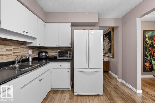 The kitchen features white cabinetry, a dark countertop, a stainless steel sink, and a white refrigerator - 3240 130A Avenue, Edmonton, AB - Indoor Photo Showing Kitchen With Double Sink
