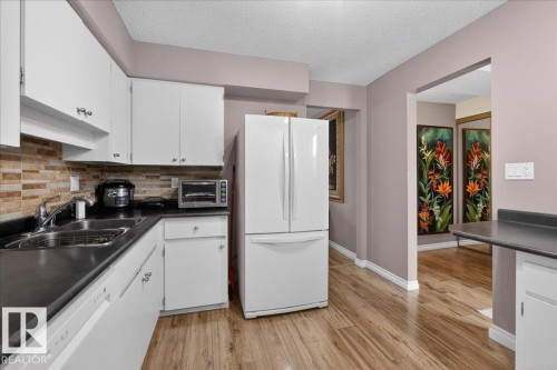 The kitchen features white cabinetry, a double basin sink with a chrome faucet, and a stone-style backsplash - 3240 130A Avenue, Edmonton, AB - Indoor Photo Showing Kitchen With Double Sink