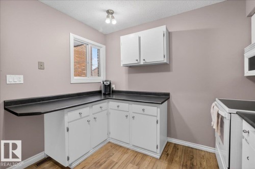 The kitchen features white cabinetry, dark countertops, and wood-look flooring - 3240 130A Avenue, Edmonton, AB - Indoor Photo Showing Kitchen