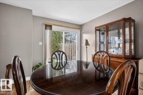 The dining area features a glass sliding door, providing natural light and a view of outdoor greenery, with a wooden dining table and chairs, and a display cabinet - 3240 130A Avenue, Edmonton, AB - Indoor