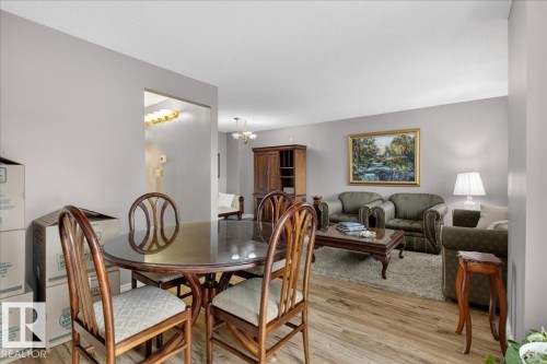 The property offers a dining area with wood flooring and a round table, open to a living area featuring a rug and a wall-mounted piece of art - 3240 130A Avenue, Edmonton, AB - Indoor Photo Showing Dining Room
