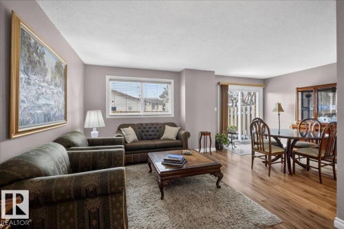 The living area features a carpeted section with a coffee table, a dining area with a table and chairs, and a sliding glass door leading to an outdoor space - 3240 130A Avenue, Edmonton, AB - Indoor Photo Showing Living Room
