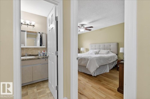 The property features a bedroom with hardwood flooring and a ceiling fan, and an adjoining bathroom with a vanity, sink, and tiled flooring - 3240 130A Avenue, Edmonton, AB - Indoor Photo Showing Bedroom