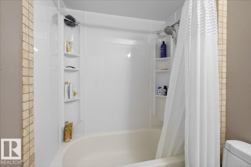 The bathroom features a bathtub and shower combination unit with integrated shelving, accompanied by a shower curtain and tiled wall accents - 3240 130A Avenue, Edmonton, AB - Indoor Photo Showing Bathroom