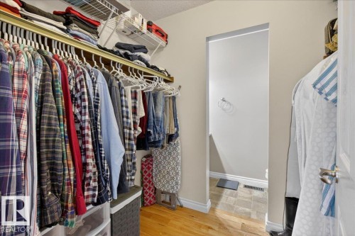 This walk-in closet features hardwood flooring, built-in shelving, and a doorway leading to an additional space with tiled flooring - 3240 130A Avenue, Edmonton, AB - Indoor With Storage