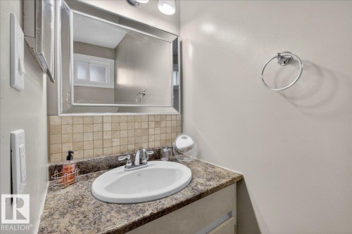 Bathroom vanity featuring a speckled countertop, an undermount sink with a chrome faucet, and a tiled backsplash - 3240 130A Avenue, Edmonton, AB - Indoor Photo Showing Bathroom
