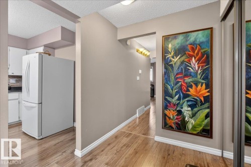 The property features wood-look flooring and a kitchen area with a white refrigerator and white cabinetry - 3240 130A Avenue, Edmonton, AB - Indoor