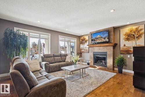 The living room features hardwood flooring, recessed lighting, and large windows providing natural light - 11409 63 Street Nw, Edmonton, AB - Indoor Photo Showing Living Room With Fireplace