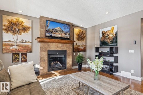 The living room features hardwood flooring, recessed lighting, and a fireplace with a stone surround and a wooden mantel - 11409 63 Street Nw, Edmonton, AB - Indoor Photo Showing Living Room With Fireplace