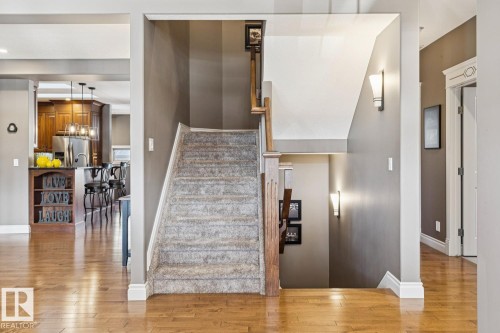 Interior view featuring hardwood floors, a carpeted staircase with a wooden railing, and wall sconces providing ambient lighting - 11409 63 Street Nw, Edmonton, AB - Indoor Photo Showing Other Room