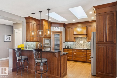 The kitchen features hardwood flooring, wooden cabinetry, and a spacious island with an integrated sink and pendant lighting - 11409 63 Street Nw, Edmonton, AB - Indoor Photo Showing Kitchen